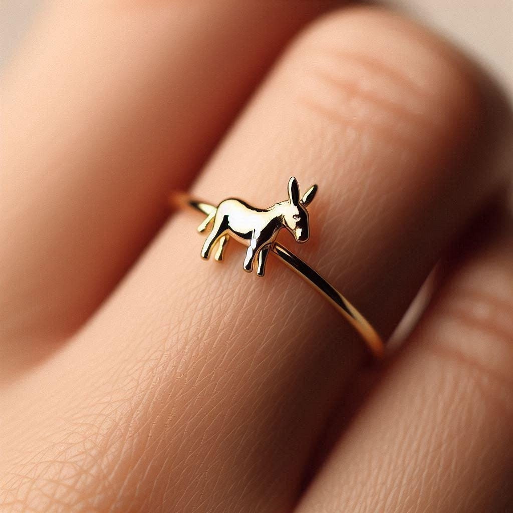 A dainty gold ring with a donkey design on a 1.5mm wide band, displayed on a person's finger.